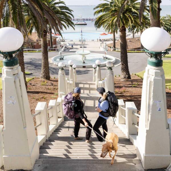 Two girls with hiking gear descending steps at Eastern Beach with their dog